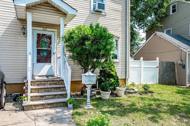 view of exterior entry with a yard, fence, and cooling unit