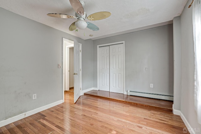 unfurnished bedroom featuring a baseboard heating unit, ceiling fan, baseboards, hardwood / wood-style floors, and a closet