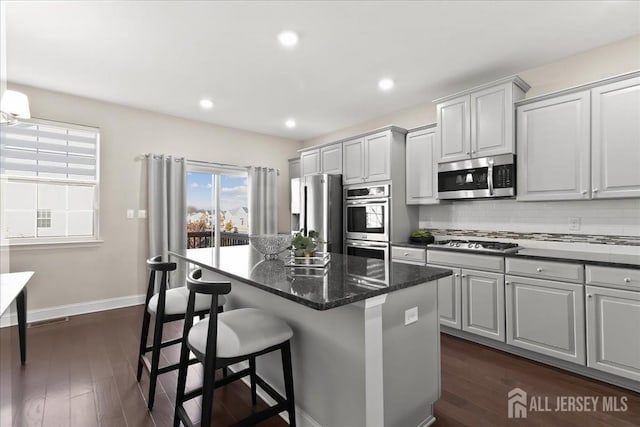 905 Chalmers Ln, Monroe, NJ 08831 - kitchen with appliances with stainless steel finishes, a kitchen island, a breakfast bar area, backsplash, and dark wood-style flooring