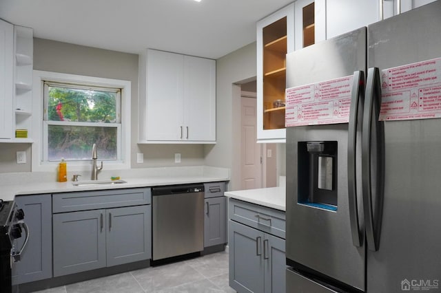 kitchen with appliances with stainless steel finishes, gray cabinetry, sink, light tile patterned floors, and white cabinets