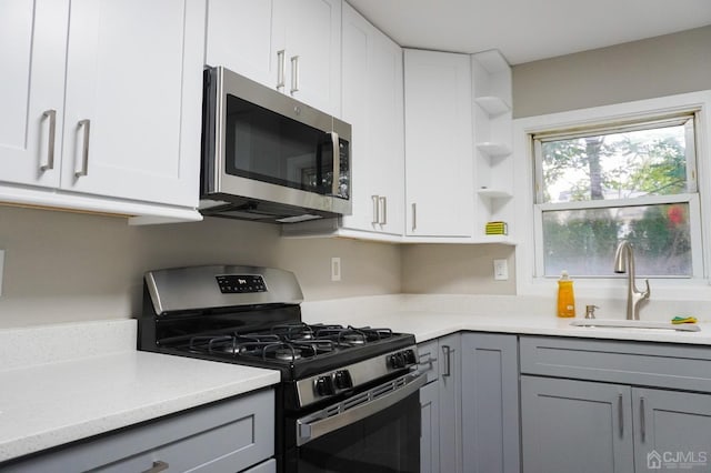 kitchen with gray cabinetry, sink, light stone countertops, white cabinetry, and stainless steel appliances