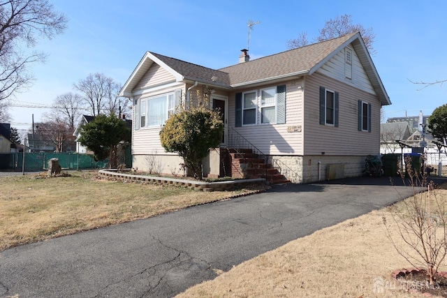 view of front of house with a shingled roof, fence, aphalt driveway, a front yard, and a chimney