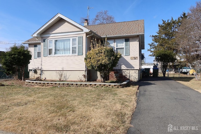 view of front of property with aphalt driveway, a chimney, a front yard, and roof with shingles