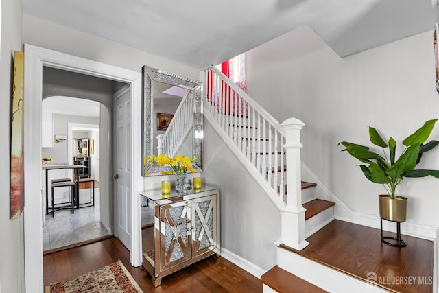 staircase featuring arched walkways, baseboards, and hardwood / wood-style floors