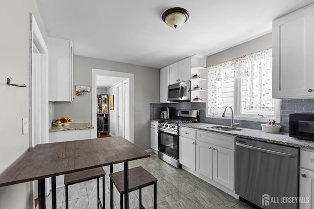 kitchen featuring decorative backsplash, appliances with stainless steel finishes, light stone countertops, open shelves, and a sink