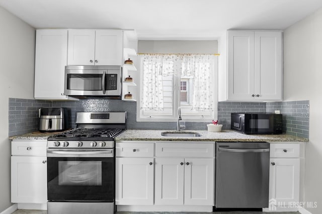 kitchen featuring light stone counters, a sink, stainless steel appliances, white cabinetry, and backsplash