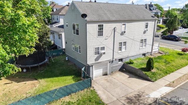 view of side of home featuring a trampoline, a shingled roof, a yard, an attached garage, and concrete driveway