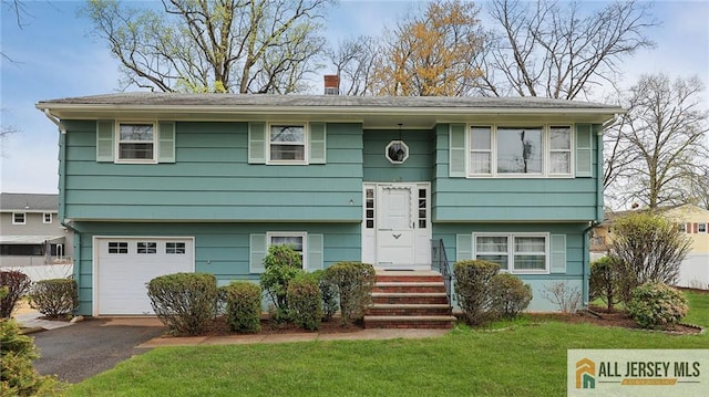 split foyer home with a chimney, driveway, a front lawn, and a garage