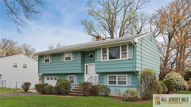raised ranch featuring a chimney, a front yard, an attached garage, and driveway