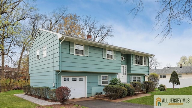 bi-level home featuring aphalt driveway, fence, an attached garage, a front yard, and a chimney