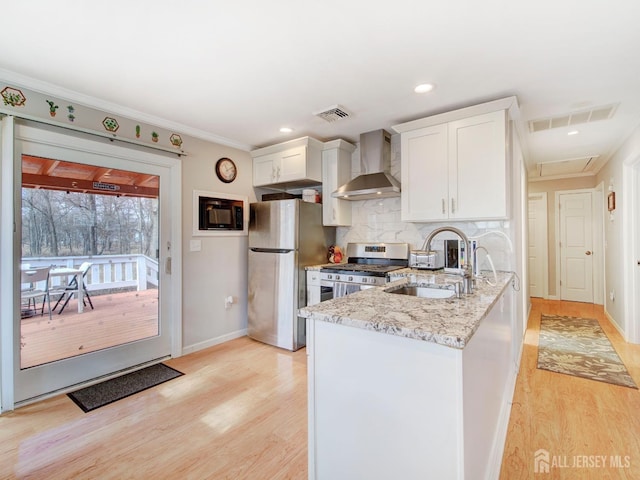 kitchen featuring sink, wall chimney range hood, stainless steel appliances, light stone countertops, and white cabinets