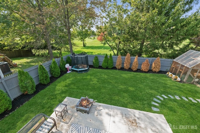 view of yard with a fire pit, a greenhouse, a fenced backyard, and an outdoor structure