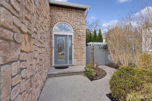 doorway to property featuring stone siding and fence