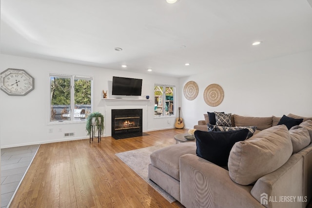 living area with recessed lighting, a fireplace with flush hearth, wood finished floors, baseboards, and visible vents