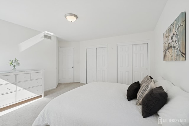 bedroom with multiple closets, light colored carpet, and visible vents