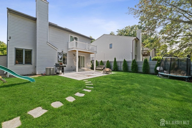 back of house with a trampoline, a chimney, a lawn, a patio area, and a balcony