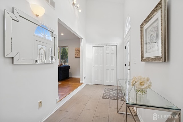 foyer featuring a towering ceiling, baseboards, visible vents, and wood finished floors