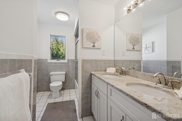 bathroom with toilet, tile patterned flooring, a sink, and wainscoting