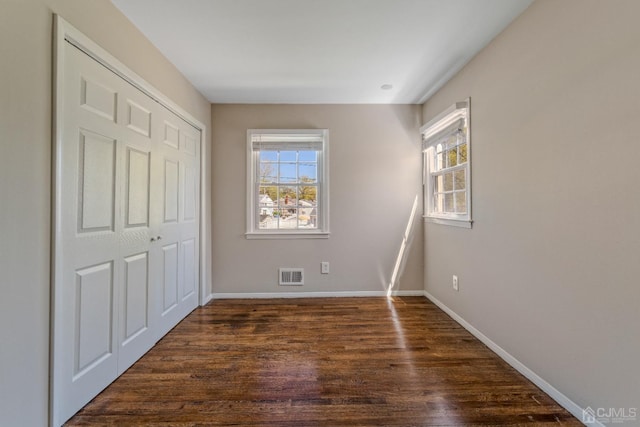 unfurnished bedroom featuring visible vents, dark wood finished floors, baseboards, and multiple windows