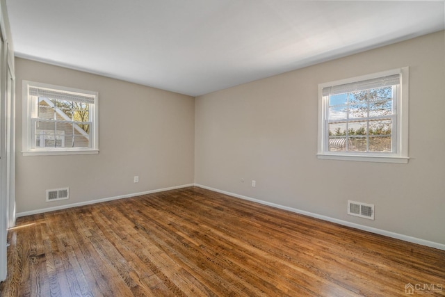 empty room featuring plenty of natural light, visible vents, and wood-type flooring