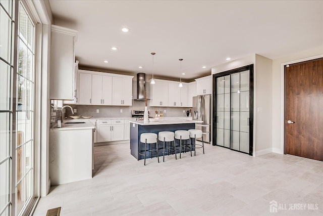 kitchen with a center island, a sink, a kitchen bar, wall chimney exhaust hood, and appliances with stainless steel finishes