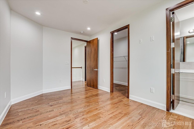 unfurnished bedroom with recessed lighting, light wood finished floors, and a walk in closet