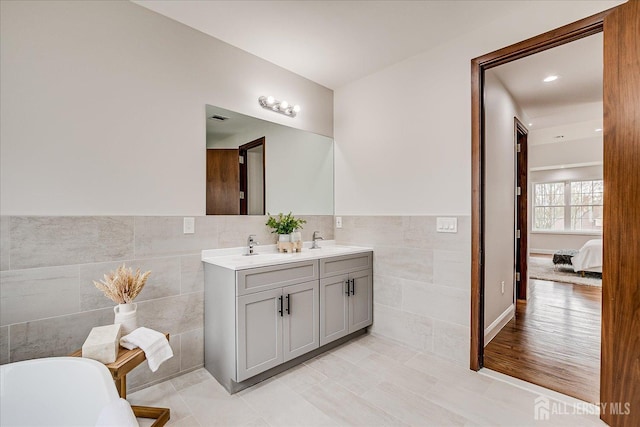 full bathroom featuring tile walls, a sink, double vanity, and a soaking tub