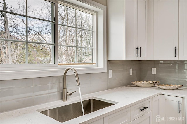 kitchen with backsplash, light stone counters, a sink, and white cabinets