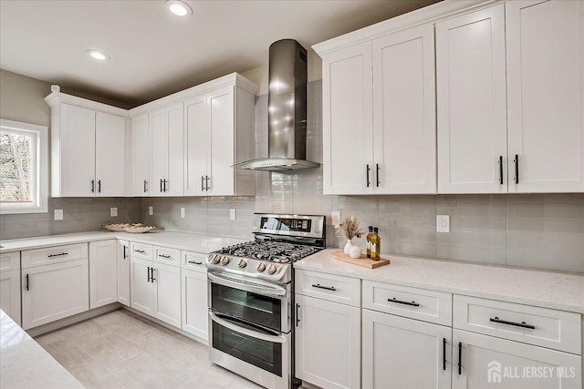 kitchen with white cabinets, light stone counters, wall chimney exhaust hood, double oven range, and decorative backsplash