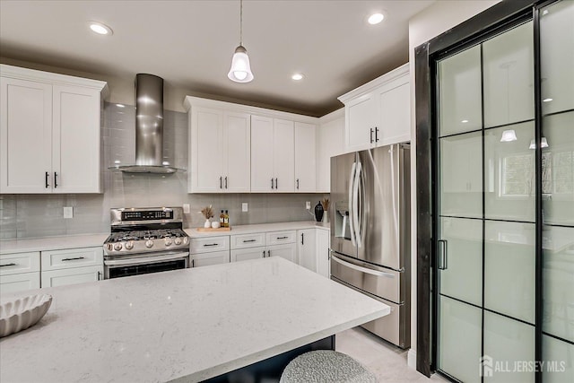 kitchen with decorative light fixtures, wall chimney range hood, white cabinets, and stainless steel appliances