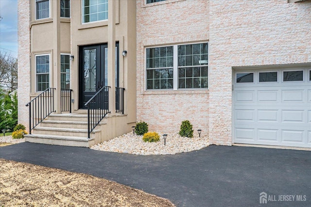 entrance to property with a garage, stucco siding, and aphalt driveway