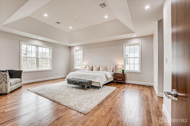 bedroom with a raised ceiling, light wood-style flooring, visible vents, and multiple windows