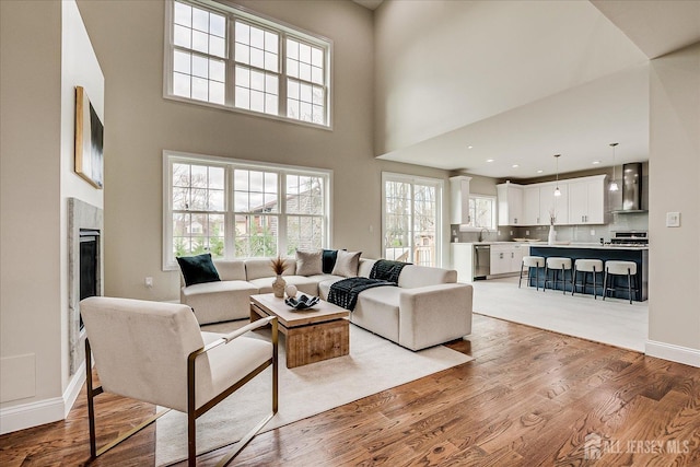 living area with a fireplace, light wood-style floors, a towering ceiling, and baseboards
