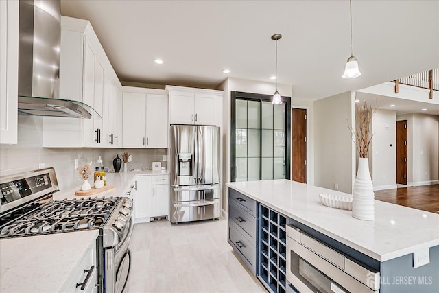 kitchen featuring white cabinets, stainless steel appliances, decorative light fixtures, wall chimney exhaust hood, and decorative backsplash
