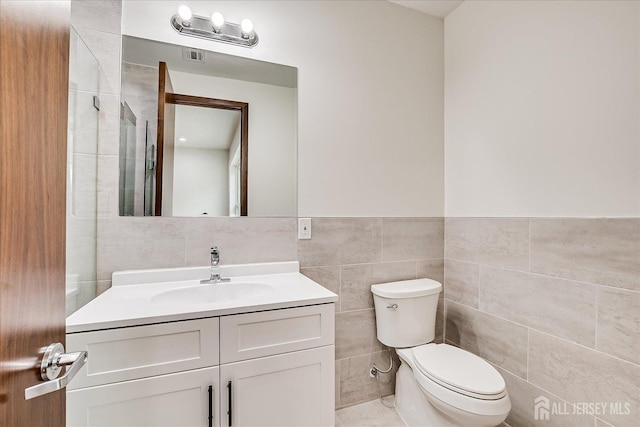 full bathroom with tile walls, a wainscoted wall, toilet, vanity, and visible vents