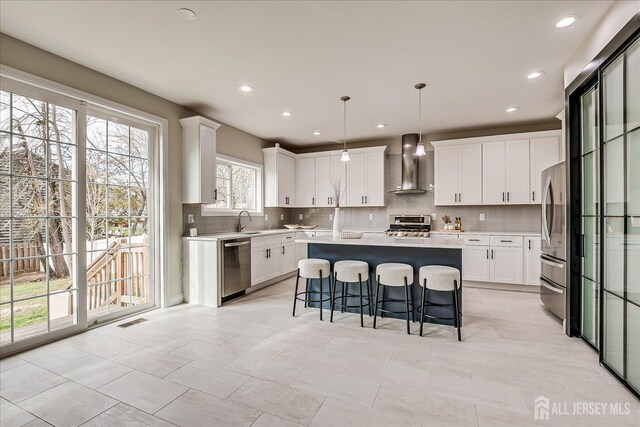 kitchen featuring stainless steel appliances, decorative backsplash, a kitchen breakfast bar, a center island, and wall chimney exhaust hood