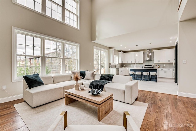 living area with light wood finished floors, a towering ceiling, and baseboards