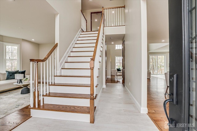 staircase featuring wood finished floors, a wealth of natural light, baseboards, and a high ceiling