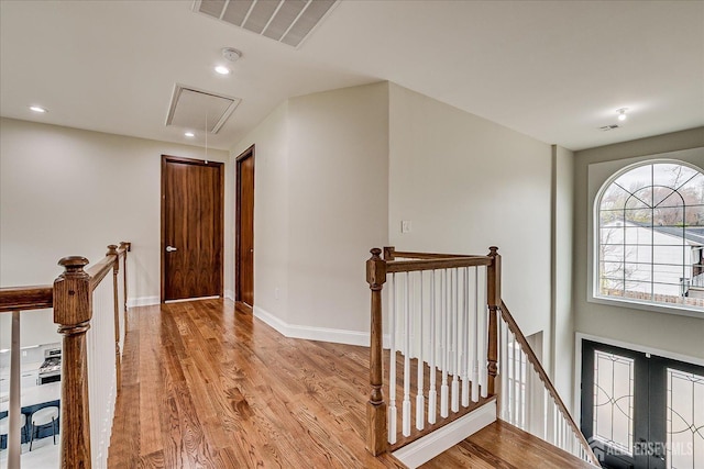 hallway with attic access, visible vents, light wood finished floors, and an upstairs landing