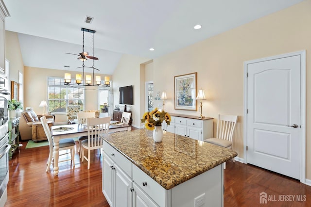 kitchen with dark wood-type flooring, white cabinetry, visible vents, a kitchen island, and lofted ceiling
