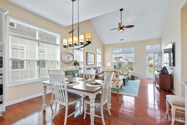 dining space with high vaulted ceiling, ceiling fan with notable chandelier, baseboards, and wood finished floors