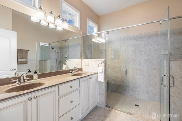 bathroom with a stall shower, double vanity, and a sink