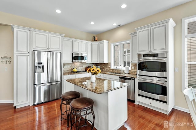 kitchen with tasteful backsplash, stone countertops, a center island, appliances with stainless steel finishes, and a sink