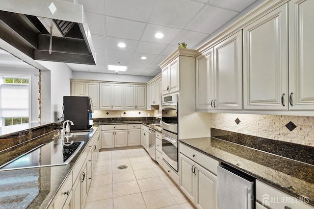 kitchen featuring dark stone countertops, light tile patterned flooring, a sink, stainless steel appliances, and backsplash