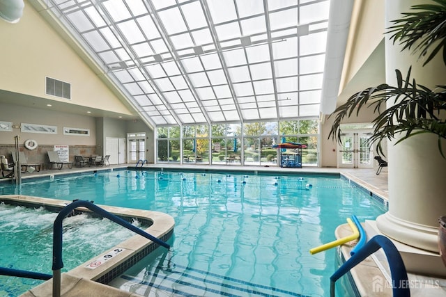 pool with a patio area, an indoor in ground hot tub, and glass enclosure