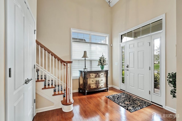 foyer entrance featuring baseboards, a towering ceiling, hardwood / wood-style flooring, and stairs