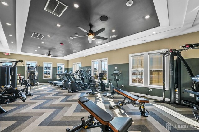 exercise room featuring a raised ceiling, carpet, and ceiling fan