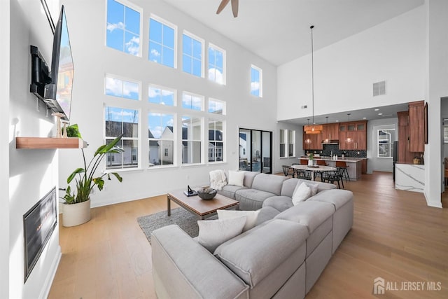 living area with a fireplace, a ceiling fan, visible vents, and light wood finished floors