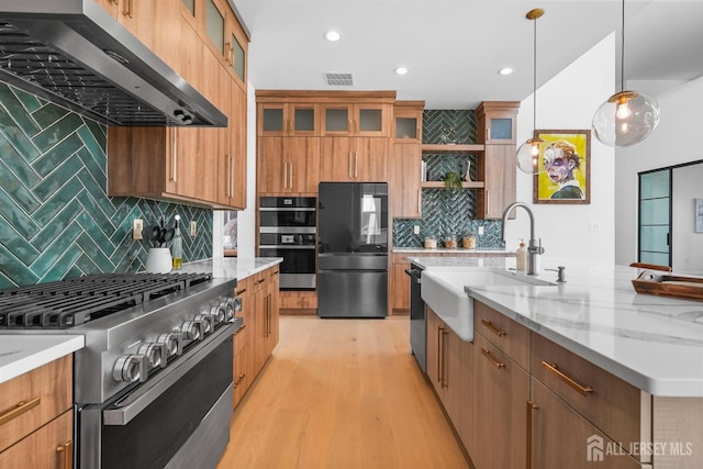 kitchen with appliances with stainless steel finishes, decorative light fixtures, sink, light stone counters, and wall chimney range hood