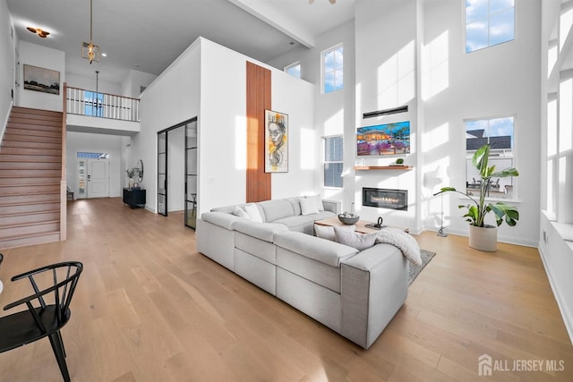 living room with a glass covered fireplace, a high ceiling, and light wood-style flooring